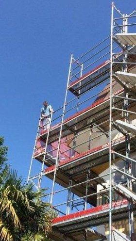 Échafaudage dressé sur plusieurs étages, un peintre au dernier niveau