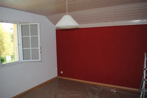 Mur rouge profond sous une suspension blanche, reste de la pièce clair