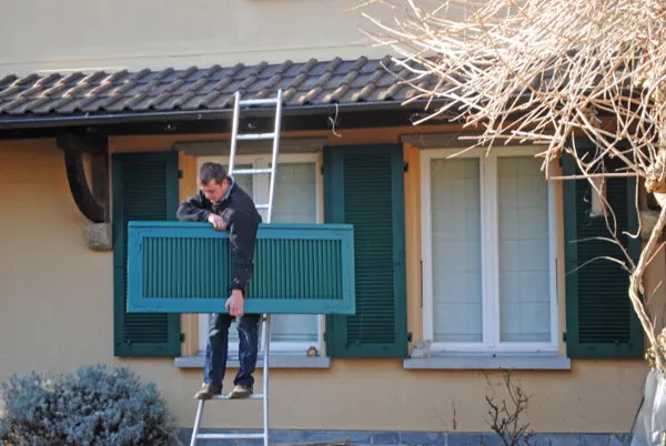 Peintre à l’échelle devant un volet bleu-vert fraîchement repeint