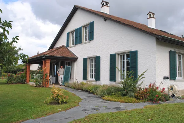 Façade blanche et volets vert sombre, jardin au premier plan